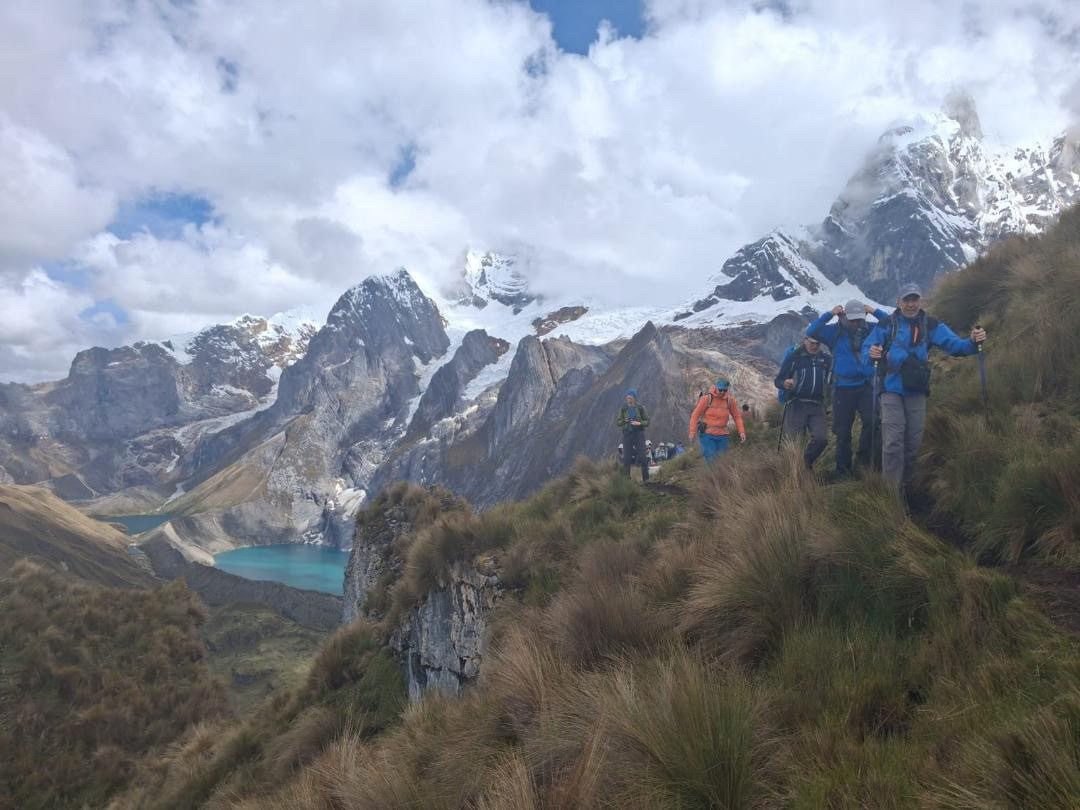 Trekkers moving in single file along a ridge crest beneath the glaciated massif.
