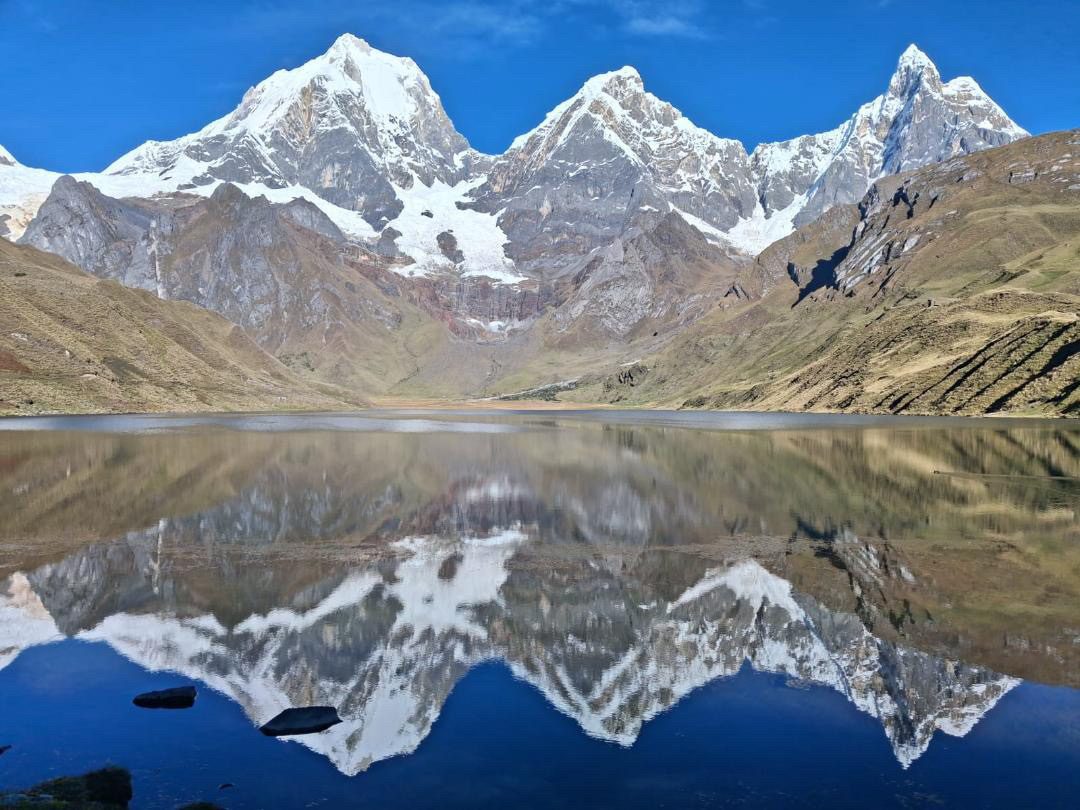 Snow peaks mirrored in the flat calm of a lake under a deep blue sky.